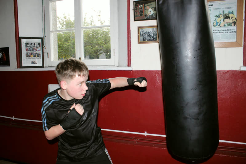 A boy working the heavy bag, newspaper cuttings behind him