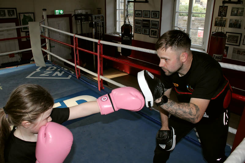 A young girl in pink gloves throwing a jab into a coach's pad