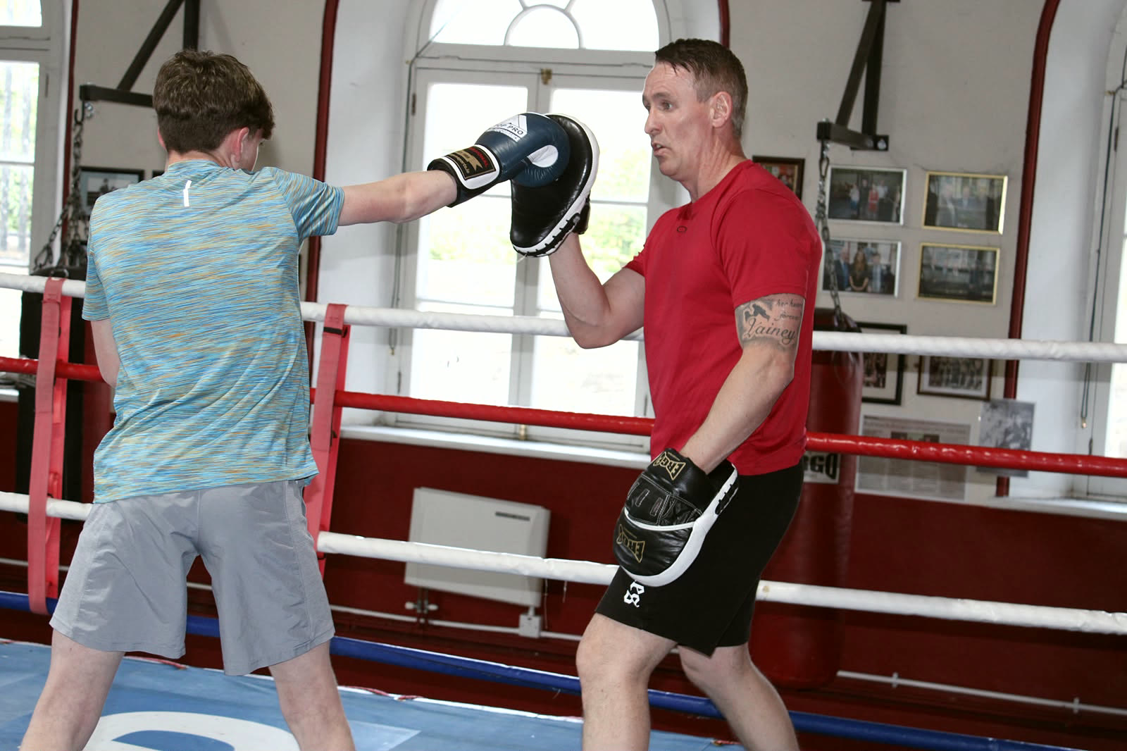 A teenager working the pads with a coach inside the ring at Arbour Hill